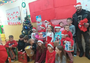 Grupowe zdjęcie z pomocnikiem Mikołaja i Mikołajem w tle