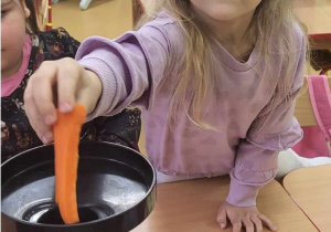 Dziewczynka wkłada marchewkę do sokowirówki